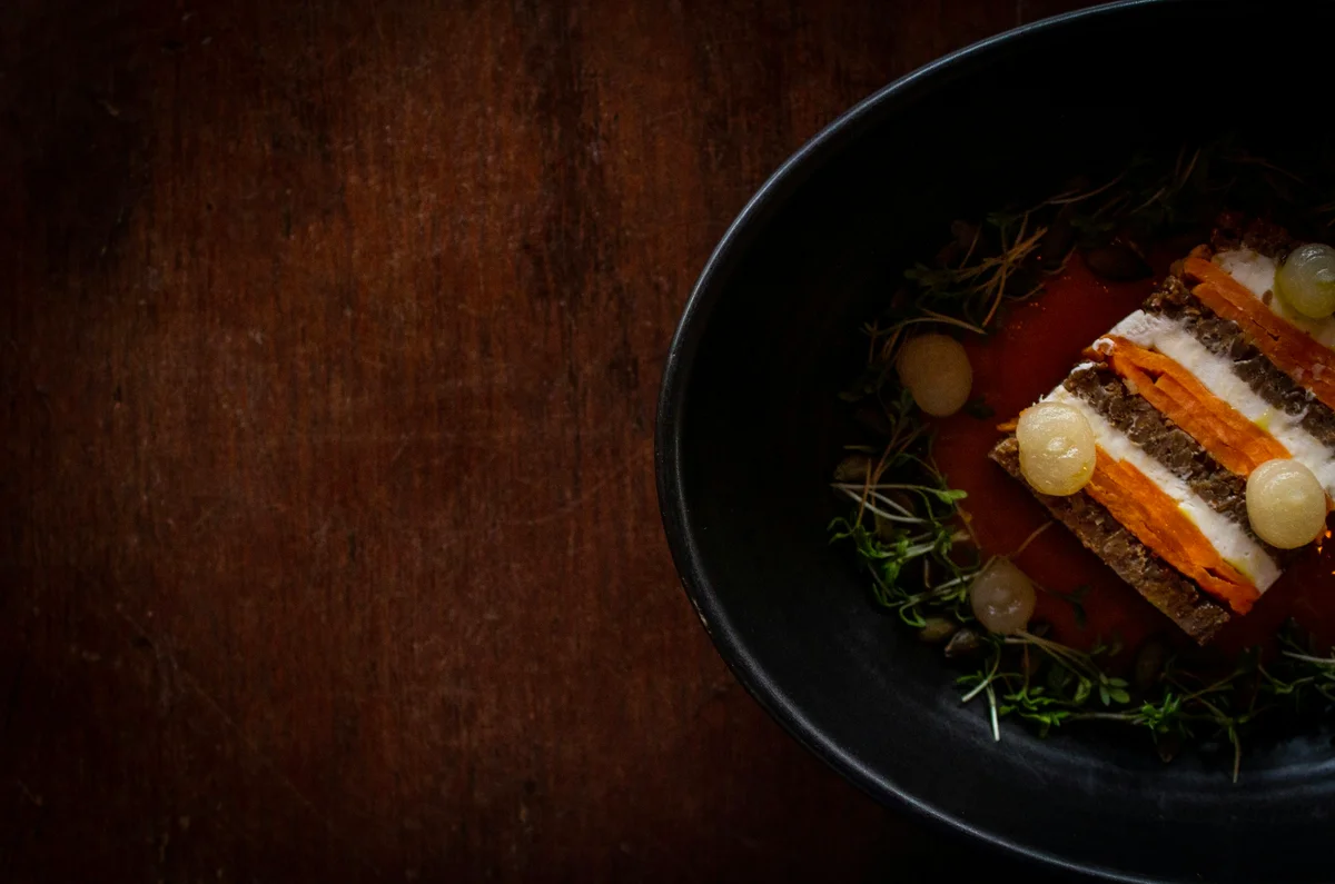 A layered vegetable terrine with herbs on a dark plate